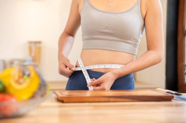 Spor kıyafetli bir kadını belinde şerit kullanarak mutfak tezgahında dikilirken çek. Ev yapımı yiyecekler, diyet planı, sağlıklı yaşam..