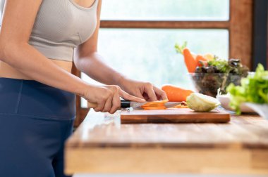 Spor giyinen kadın mutfak tezgahında havuç keserken bıçak kullanıyor. Ev yapımı yiyecekler, diyet planı, sağlıklı yaşam..