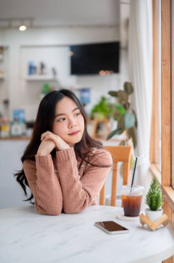 Asyalı bir kadın kafeteryada ya da kahvecide otururken ellerini tokalaştırıp dışarı bakıyor. Boş Zamanlar, Şehir Hayatı, Dışarıdaki Serinleme.