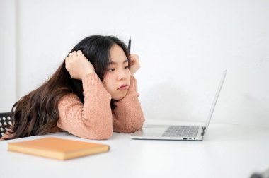 Asya 'lı bir kadın, elinde kalemle bir sınıfta ya da ofiste dizüstü bilgisayara bakıyor. Çalışma ya da Eğitim, Şehir Hayatı, Modern Teknoloji.