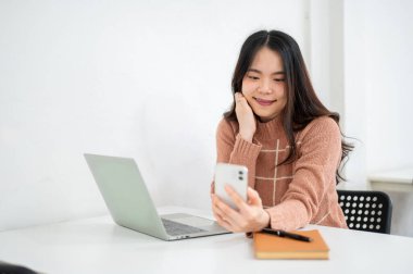 Ofiste ya da kafede beyaz odada akıllı telefonu tutan ve ona bakan Asyalı bir kadın. Çalışma ya da Eğitim, Şehir Hayatı, Modern Teknoloji.