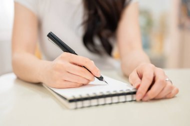 Genç bir bayanın elinde kalemle yatak odasında otururken deftere yazarken yakın çekim. Rahatlatıcı, boş zaman, evde dinlenme.