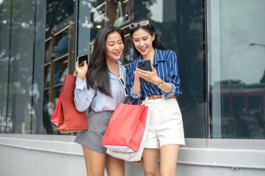 Alışveriş merkezinin dışında yürürken arkadaşına telefonunu gösteren güzel bir Asyalı kadın. Maaş günü, tanıtım reklamı, modern şehir hayatı..