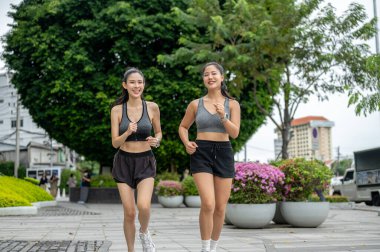 Spor giyimli Asyalı bayan arkadaşlar alışveriş merkezinin bahçesindeki kaldırımda koşu ya da koşu yaparak egzersiz yapıyorlar. Çalışmak, Sağlıklı Yaşam, Kentsel Kamu Alanı.