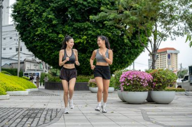 Spor giyimli Asyalı bayan arkadaşlar bahçede ya da parkta koşarak ya da koşu yaparak egzersiz yapıyorlar. Çalışmak, Sağlıklı Yaşam, Kentsel Kamu Alanı.