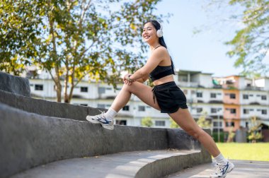 Spor giyimli Asyalı bir kadın bahçede ya da parkta çimento merdivenlerinde ısınma hareketleri yapıyor. Spor yapıyor, sağlıklı yaşıyor, dışarıda takılıyor..