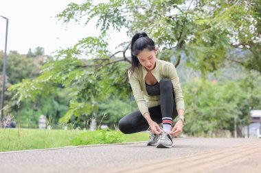 Spor kıyafetli Asyalı bir kadın yolda koşmadan önce spor ayakkabısının bağcıklarını bağlıyor. Spor yapıyor, sağlıklı yaşıyor, dışarıda takılıyor..