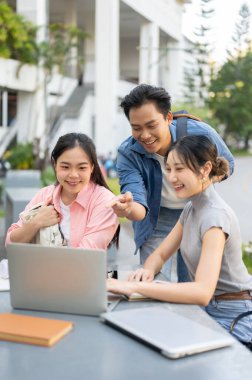 Dizüstü bilgisayara bakan Asyalı bir öğrenci üniversitede masa başında çalışan bir kadına yardım ediyor. Üniversite, Kampüs Hayatı, Modern Teknoloji.