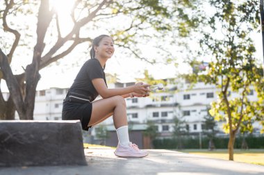 Parktaki egzersizden sonra beton merdivenlerde oturan siyah spor kıyafetli, kulaklık takan Asyalı bir kadın. Sağlıklı Yaşam, Spor, Kentsel Modern Yaşam