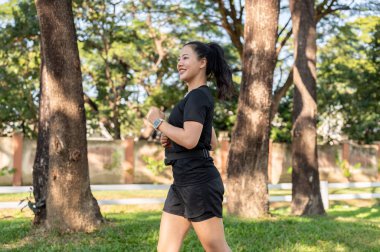 Siyah spor giyim giymiş güzel Asyalı kadın güneşli bir günde parkta koşarak ya da koşu yaparak egzersiz yapıyor. Sağlıklı Yaşam, Spor, Kentsel Modern Yaşam
