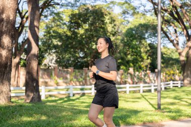 Siyah spor kıyafetli güzel bir Asyalı kadın güneş ışığında koşuyor ya da parkta koşuyor. Sağlıklı Yaşam, Spor, Kentsel Modern Yaşam