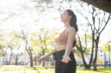 Spor giyim kuşamında güzel bir Asyalı kadın gözlerini kapatıyor. Parktaki egzersizden sonra ya ayakta duruyor ya da dinleniyor. Sağlıklı Yaşam, Spor, Kentsel Modern Yaşam