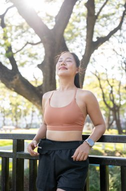 Spor giyimli güzel Asyalı kadın parktaki egzersizden sonra korkuluklara yaslanmış gözlerini kapadı. Sağlıklı Yaşam, Spor, Kentsel Modern Yaşam