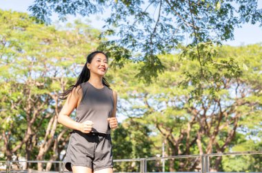 Spor giyimli güzel bir Asyalı kadın koşuyor ya da güneş ışığı altında yeşil parkta koşuyor. Sağlıklı Yaşam, Spor, Kentsel Modern Yaşam