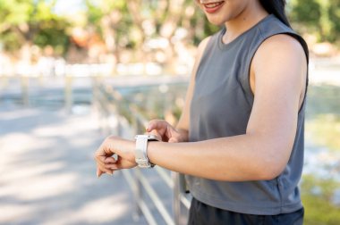 Spor kıyafetli bir kadının park alanında egzersiz yaparken ayakta dikilip saatlere baktığı bir sahne. Sağlıklı Yaşam, Spor, Kentsel Modern Yaşam