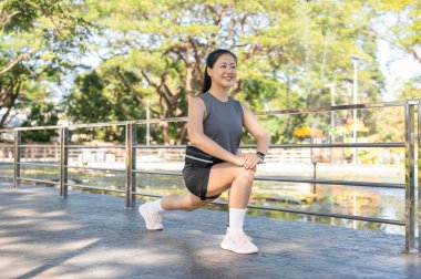 Spor kıyafetli güzel bir Asyalı kadın eğilmiş bacak kaslarını bir kenara bırakıp parkta korkuluklara tırmanıyor. Sağlıklı Yaşam, Spor, Kentsel Modern Yaşam