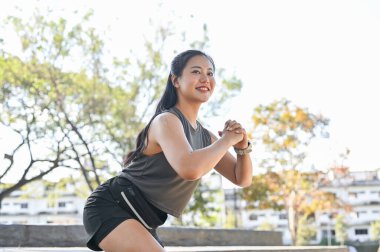 Spor giyimli güzel bir Asyalı kadın bahçede çömelip spor yapıyor ya da güneşli bir parkta. Sağlıklı Yaşam, Spor, Kentsel Modern Yaşam