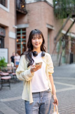 Alışveriş merkezinde ya da markette yürürken elinde içki ve telefon tutan Asyalı kadın turist. Tek başına yolculuk, şehir turu, açık havada dinlenme..