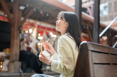 Alışveriş merkezinde ya da markette bankta otururken hindistan cevizi suyu içen güzel Asyalı kadın turist. Tek başına yolculuk, şehir turu, açık havada dinlenme..