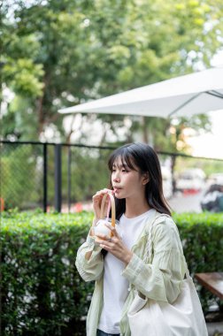 Güzel Asyalı kadın turist elinde samanla alışveriş merkezinde yürürken hindistan cevizi suyu içiyor. Tek başına yolculuk, şehir turu, açık havada dinlenme..