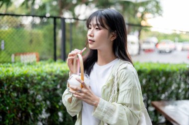 Güzel Asyalı turist elinde saman tutarken alışveriş merkezinde oturmuş hindistan cevizi suyu içiyor. Tek başına yolculuk, şehir turu, açık havada dinlenme..