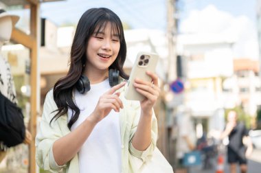 Güzel Asyalı kadın turist ayakta dururken ya da dükkanda dolaşırken akıllı telefona bakıyor. Tek başına yolculuk, şehir turu, açık havada dinlenme..