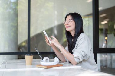 Gözlüklü Asyalı bir üniversite öğrencisi laptoptan gözünü kaçırıp binadaki masada oturuyor. Boş zaman, Üniversite Kampüsü, Şehir Hayatı.
