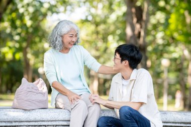 Yaşlı kadın büyükanne bahçede ya da parkta taş bir bankta otururken genç bir adama gülümsüyor. Aile Bağları, Seyahat Gezisi, Serinlemek Açık Hava.