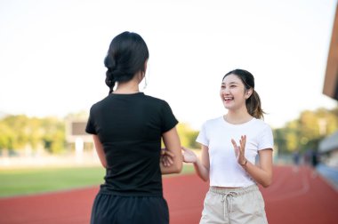 Güzel Asyalı bir kadın spor stadyumunda koşmadan ya da antrenman yapmadan önce arkadaşıyla konuşuyor. Spor, sağlıklı yaşam, açık hava aktivitesi.