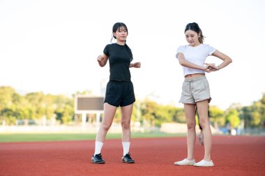 Stadyumdaki yarış pistinde koşmadan önce spor kıyafetleriyle kas geren Asyalı bir bayan arkadaş. Spor, sağlıklı yaşam, açık hava aktivitesi.