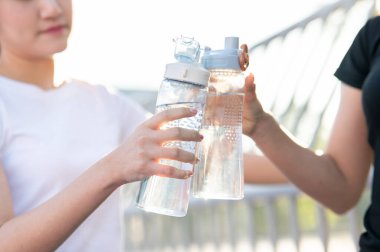 Spor stadyumunda egzersiz yaptıktan sonra bir kadının ellerini su şişesini tutarken kapatın. Spor, sağlıklı yaşam, açık hava aktivitesi.