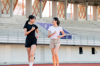 Asyalı bayan arkadaşlar yarış pistinde koşmak ya da koşu yapmak olarak konuşuyorlar. Spor stadyumunda egzersiz yapıyorlar. Spor, sağlıklı yaşam, açık hava aktivitesi.