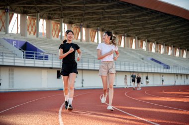 Mutlu Asyalı bayan arkadaş yarış pistinde birlikte koşuyor spor stadyumunda egzersiz yapıyor. Spor, sağlıklı yaşam, açık hava aktivitesi.