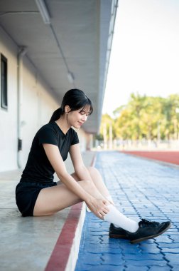 Spor ayakkabısı ve spor ayakkabısı giymiş güzel Asyalı bir kadın spor stadyumunda oturmuş gibi çorap ayarlıyor. Spor, sağlıklı yaşam, açık hava aktivitesi.