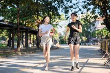 Güzel Asyalı kadın parkta koşarken ya da yolda koşarken arkadaşına bakıyor. Spor, sağlıklı yaşam, açık hava aktivitesi.