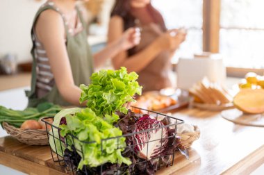 Mutfak tezgahında taze sebze malzemesiyle yemek pişiren bulanık kadın arkadaşını yakından çek. Sağlıklı İlişkiler, Ev Yapımı, Dengeli Yaşam.