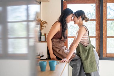 Güzel Asyalı kadın mutfak tezgahında oturan kız arkadaşıyla alnına dokunuyor. Sağlıklı İlişkiler, Birlikte Yaşam, Denge Yaşamı.