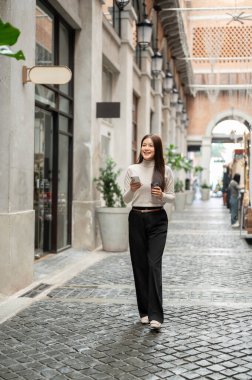Asyalı kadın elinde kahve fincanı ve telefon tutarken alışveriş merkezinde ya da markette dolaşırken. Boş zaman, Solo gezi, Seyahat Turisti.
