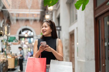 Alışveriş merkezinin ya da marketin önünde elinde telefonla bekleyen Asyalı güzel bir kadın. Boş zaman, Solo Seyahat, Turist Satın Alma.
