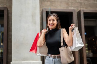 Güzel Asyalı bir kadın alışveriş merkezinde ya da markette yürürken ya da ayakta dururken iki elinde alışveriş torbaları taşıyor. Eğlence Zamanı, Seyahat Gezisi, Müşteri Alımı.