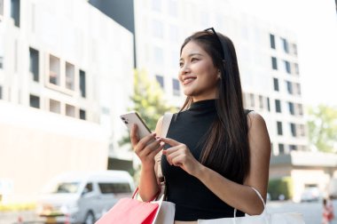 Elinde alışveriş poşetleri taşıyan Asyalı güzel bir kadın ayakta dururken ya da yolda yürürken. Boş zaman, Solo Seyahat, Turist Satın Alma.