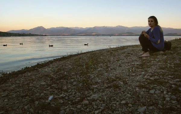 Женщина с темными волосами сидит на тихом берегу озера — стоковое фото