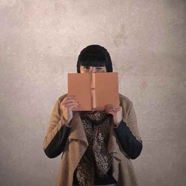 Mujer de pelo oscuro se esconde detrás de un libro —  Fotos de Stock