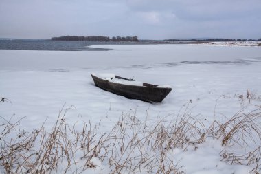 Gölün karlı kıyısında karla kaplı bir tekne..