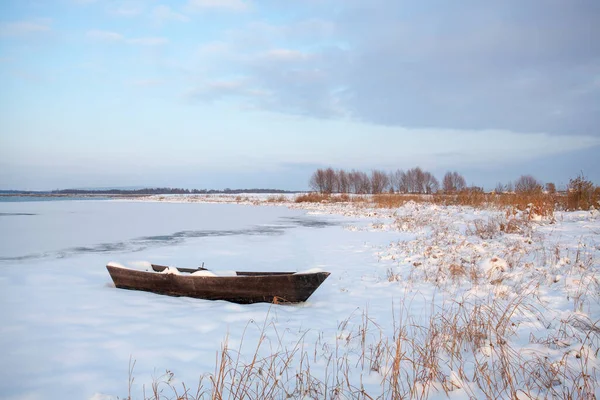 A boat covered with snow on the snowy shore of the lake.