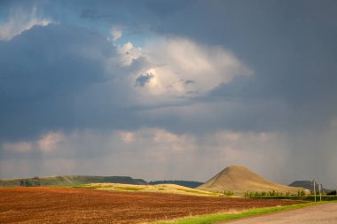 İki tenha dağ, küçük bir orman parçası ve ön planda ekilebilir arazi, çok anlamlı bir akşam ışığı ve dramatik gökyüzü olan tepelik bir bölge..