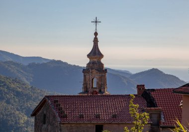 Tapınağın çan kulesi dağların arka planında, kiremit çatılı evlerle çevrili..