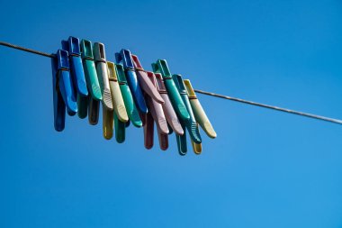 Multicolored clothespins on a rope against the blue sky.