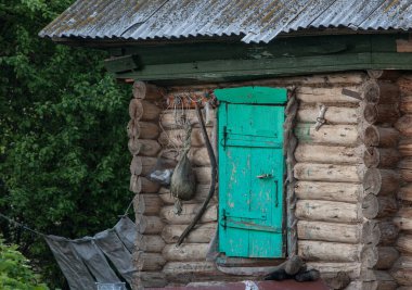 Yeşil kapılı bir kütük kulübesi. Ahırın duvarlarına çeşitli ev eşyaları asılmış..