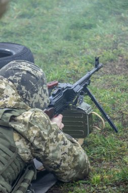 Kamuflaj üniformalı makineli tüfek operatörü ve çelik yelek Kalaşnikof makineli tüfeğiyle atış pozisyonunda. Savaş konsepti için çekim ve eğitim